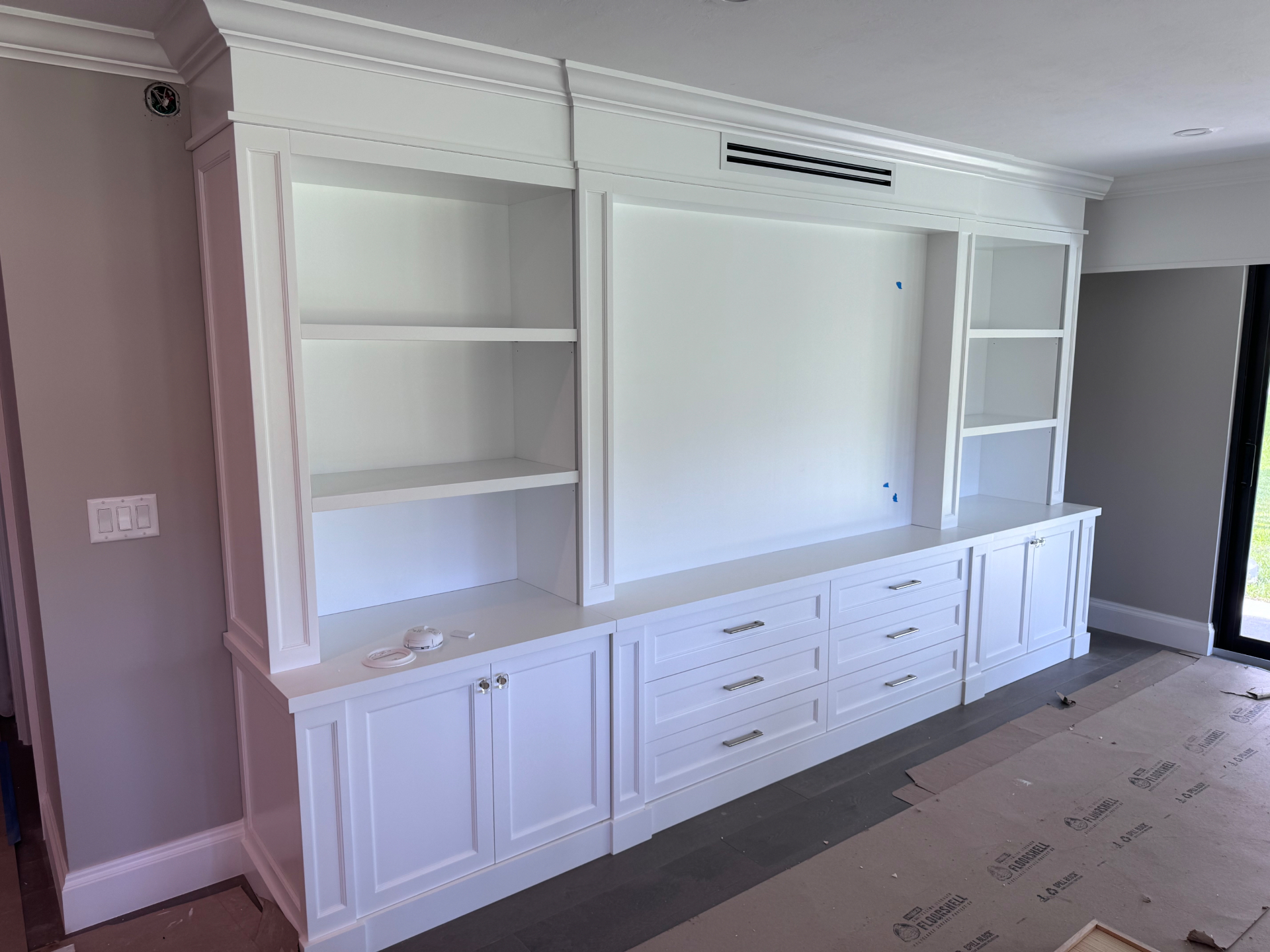 Full-wall white entertainment center with crown molding, open shelving and paneled base cabinets