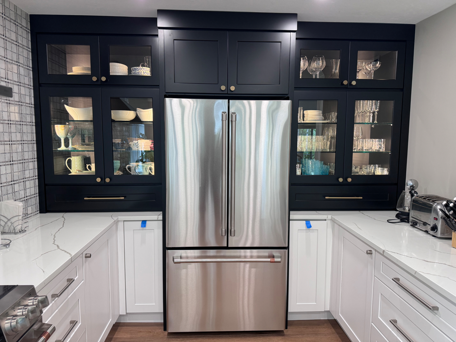 Navy glass-front display cabinetry with integrated lighting flanking a paneled refrigerator surround